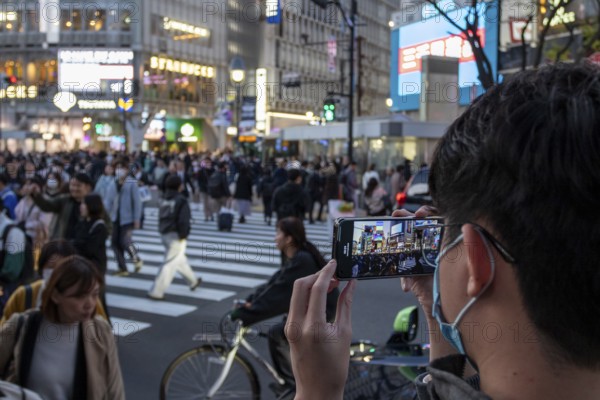 A tourist films the crowd at the zebra crossing of Shibuya Crossing with his smartphone,