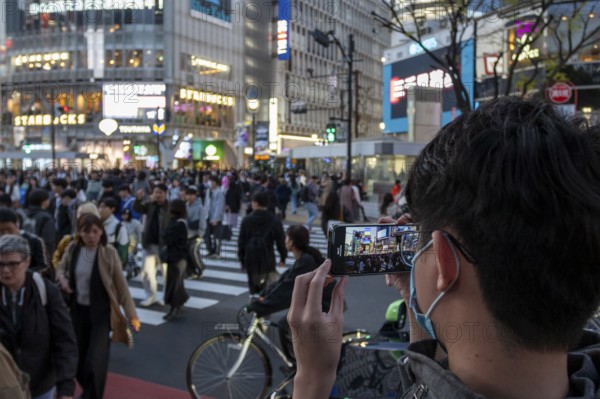 A tourist films the crowd at the zebra crossing of Shibuya Crossing with his smartphone,