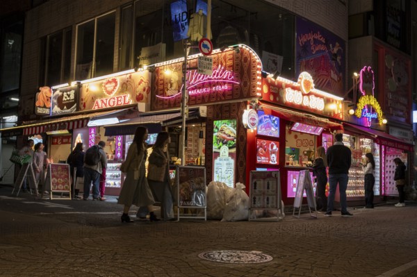Tourists in front of a shop with illuminated advertisement for kebab and Japanese crepes in