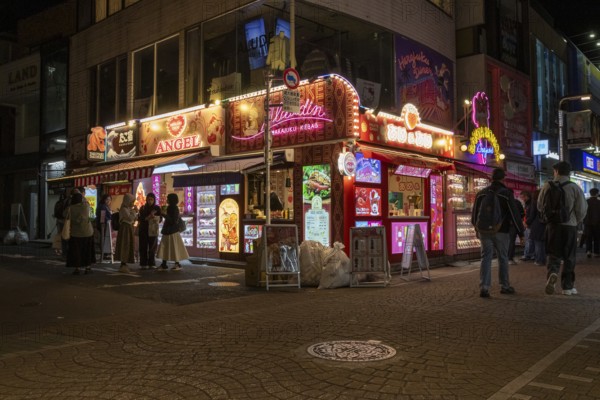 Tourists in front of a shop with illuminated advertisement for kebab and Japanese crepes in