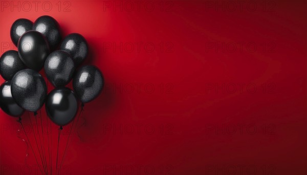 A cluster of black balloons floats against a bold red background, representing celebration, party,