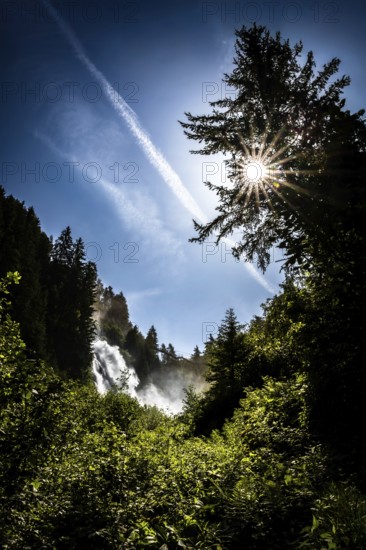 A waterfall in the forest under a bright sun and blue sky. Stuibenfall Austria Ötztal