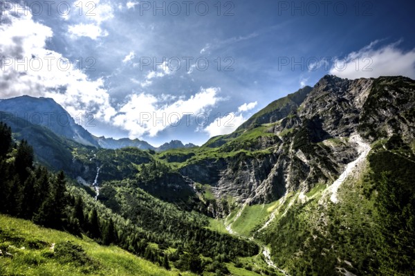 Sunny mountain scene with green slopes and dramatic clouds over the mountains. Kleinwalsertal