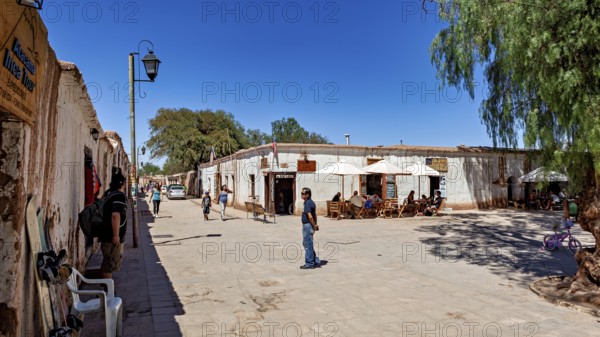 People sit under umbrellas on a lively street next to typical local buildings in the sunshine, The
