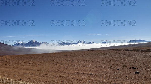 Dry desert plain with distant mountains and wafts of mist under a clear sky, The landscape at San