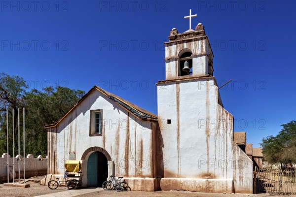Historic church with bicycle in front of a clear blue sky, cross on the bell tower, The church of