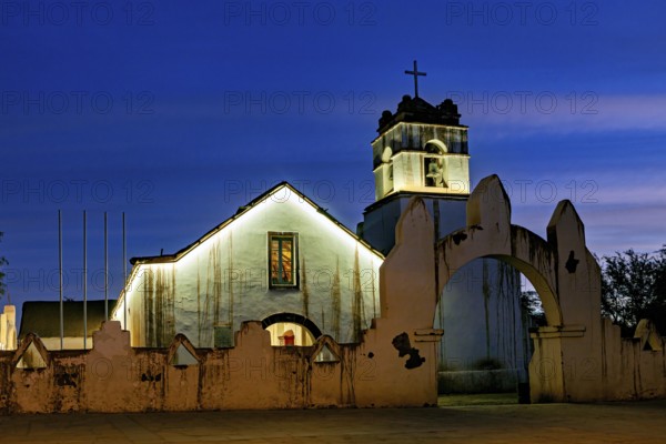 Church at dusk with illuminated tower and cross in front of a deep blue sky, The church of San