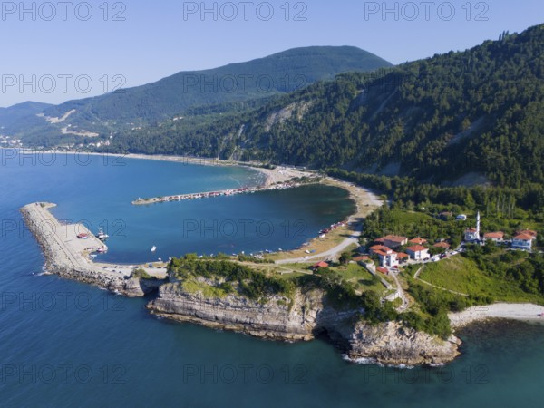 Coastal view with pier and green hills, surrounded by clear sea and scattered houses, aerial view,