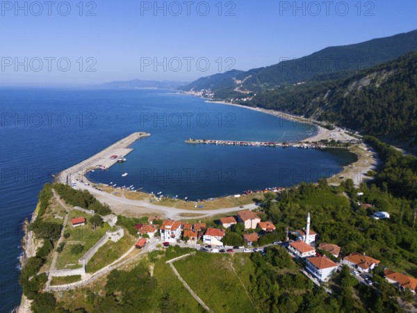 Aerial view of a coastal town with red roofs surrounded by green hills and calm blue sea, aerial