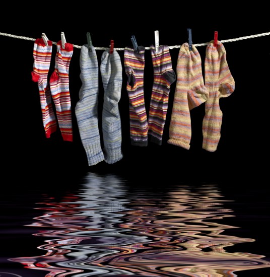 Clothesline with some multicolored sox fixed with clothes pins over reflective water surface in