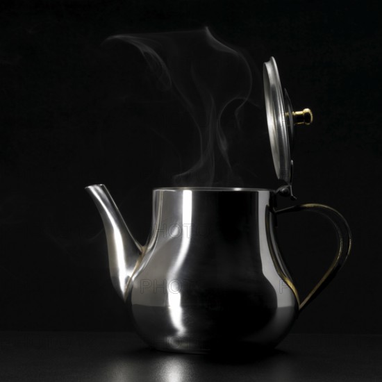 Studio photography of a steaming metal tea pot in dark back