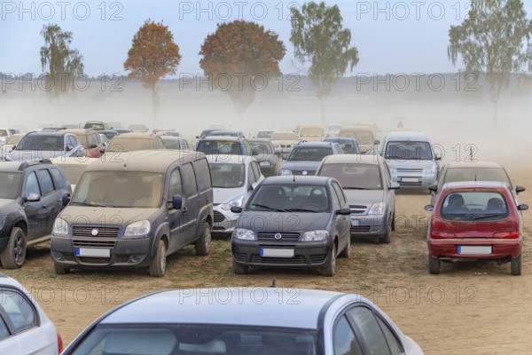 Dusty parking space scenery on a field including lots of dust covered cars at evening time in