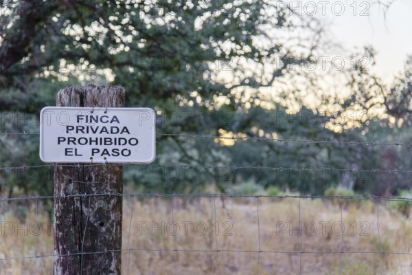 No trespassing sign in spanish (finca privada, prohibido el paso) attached to a barbed wire fence