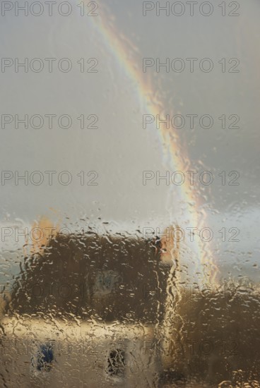 A house seen through a rain-soaked window with a rainbow arching across a gray sky, Old house