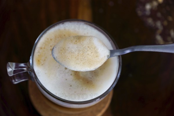 Creamy coffee foam being lifted by a spoon from a glass cup, creating a close-up view of the rich