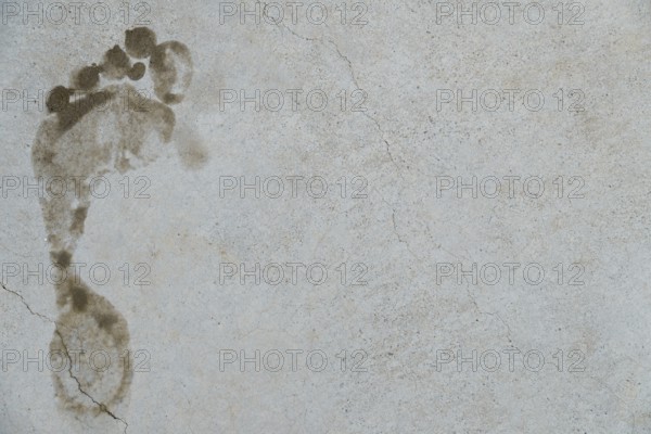 Muddy footprint marking a gray concrete surface with cracks, symbolizing evidence, trace, or