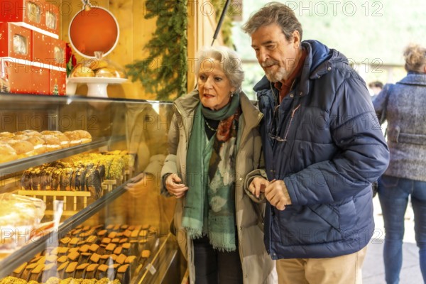 Elderly couple choosing christmas cakes and pastries at an outdoor market during the winter