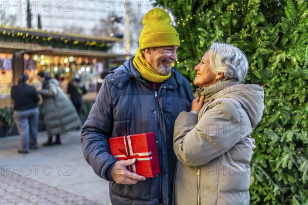 Loving senior couple exchanging christmas gifts at a festive outdoor market, enjoying the holiday