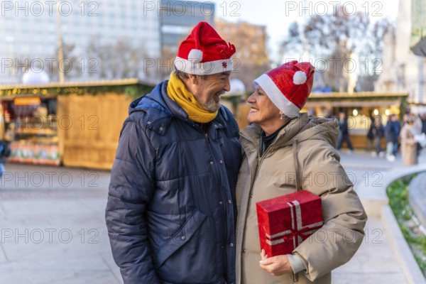 Loving senior couple wearing santa hats exchanging christmas gifts at a christmas market in the