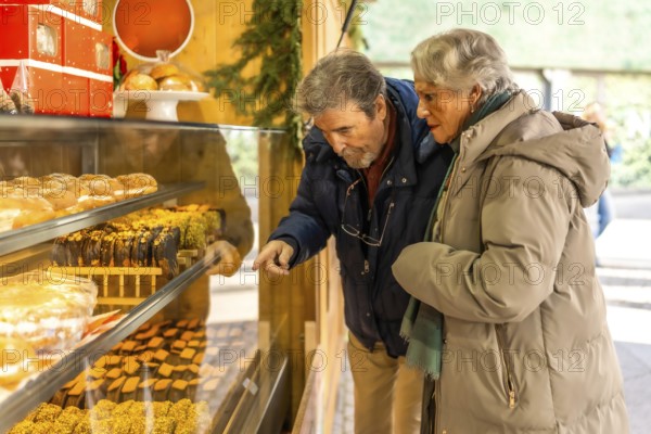 Elderly couple pointing and choosing delicious pastries from a market stall display during the