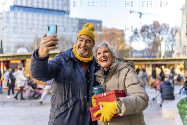 Cheerful senior couple taking a selfie with smartphone at a christmas market, holding gifts and