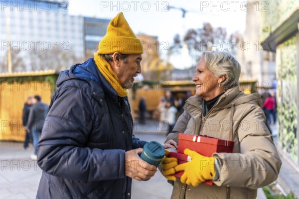 Happy senior couple exchanging christmas gifts and enjoying a warm beverage at a bustling outdoor