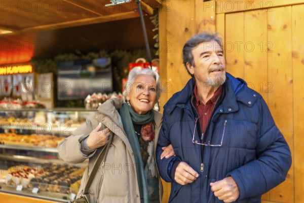 Happy senior couple strolling arm in arm at a traditional christmas market, enjoying the festive