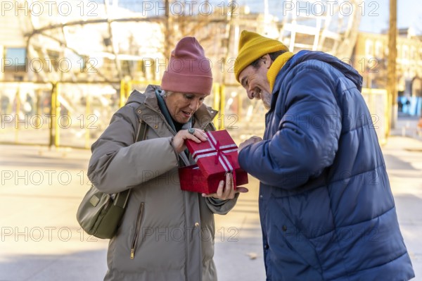 Happy senior couple sharing a joyful moment while opening a festive christmas gift box in a