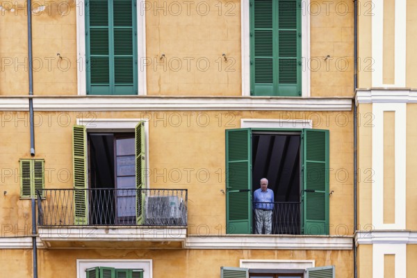 Senior man standing and looking out of an open window in an apartment house, Palma de Mallorca,