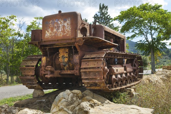 Old, heavily rusted bulldozer for road construction stands abandoned on rocks, industrial relic