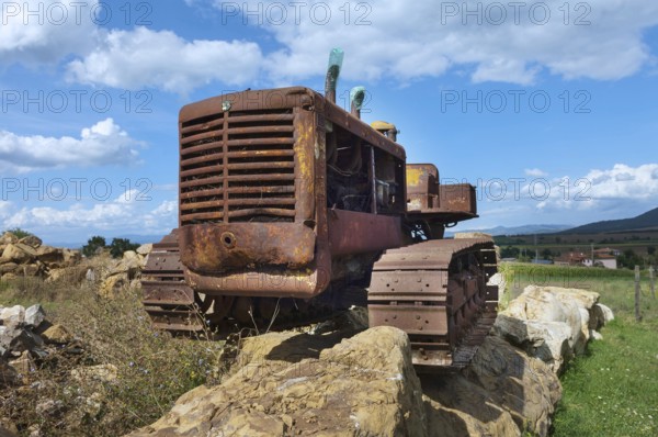 Old, heavily rusted bulldozer for road construction stands abandoned on rocks, industrial relic
