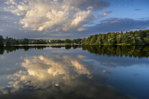 The Postfelden reservoir in the evening at the golden hour. Glowing clouds are reflected in the