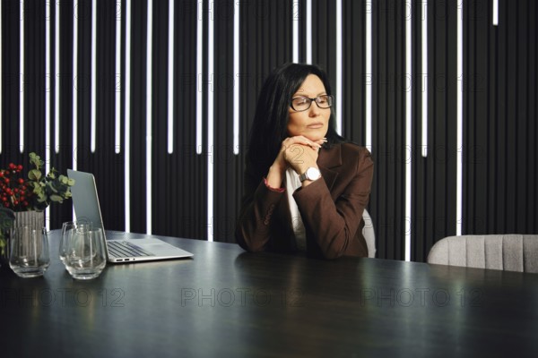 A professional woman sits at a modern desk in an elegant office space. She rests her chin on her