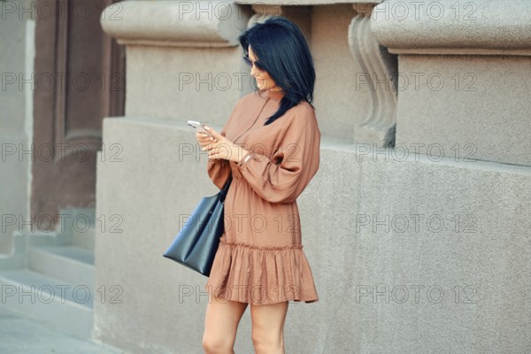 A cheerful woman stands on the street and watching as an online taxi ordered through a smartphone