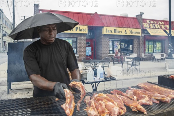 Detroit, Michigan - Wearing an umbrella, a worker places pork on the grill at Bert's Market Place