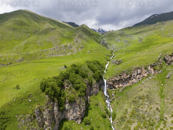 Landscape with long waterfall between green mountains under a cloudy sky, aerial view, Toti
