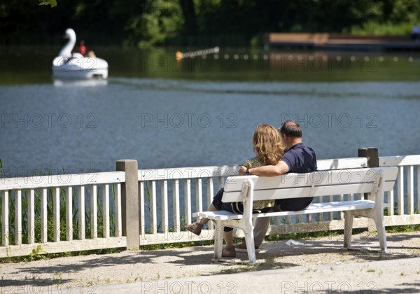 Couple sitting on a wooden bench and looking at the spa pond in the spa gardens, Großer Teich, Bad