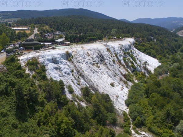 A limestone hillside overlooked by a wooded area under a blue sky, aerial view, Akkaya Travertines,