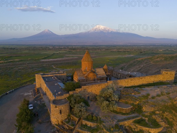 Historic monastery with surrounding wall and view of Mount Ararat at sunrise, aerial view, Chor