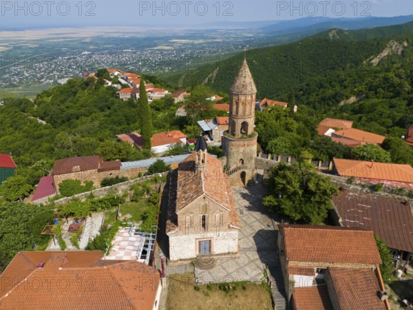 Historic church with tower in a village surrounded by mountains with red tiled roofs, aerial view,