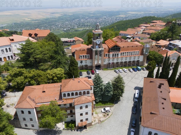 Square with a dominant tower and traditional buildings surrounded by green hills, aerial view,