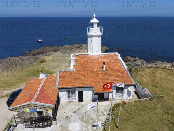 A lighthouse with terracotta roof on a rocky coast with flags and a wide ocean in the background,