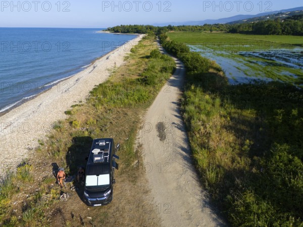 A van parked on a beach along a coastal road with lush vegetation and sea view, aerial view,