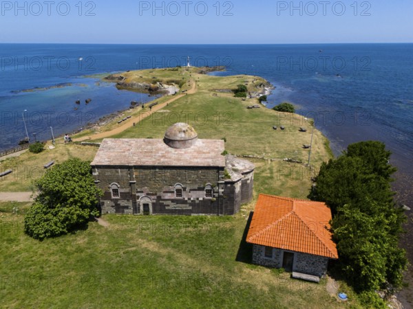 Aerial view of a historic church on the coast with neighbouring building and wide sea horizon,