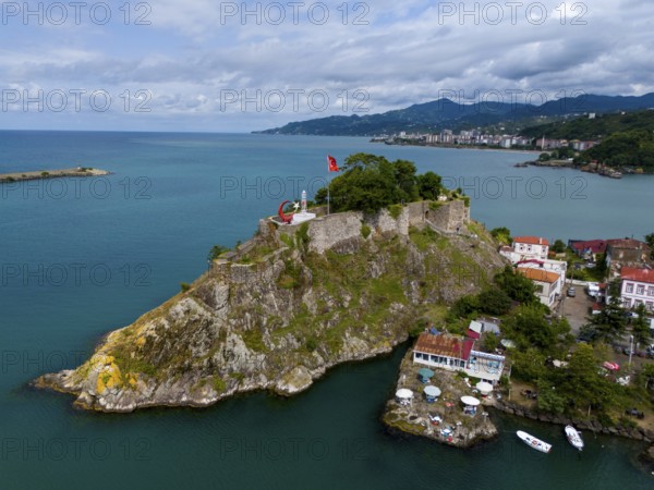 Castle on a rock formation near coastal houses and mountains with clouds, aerial view, fortress,
