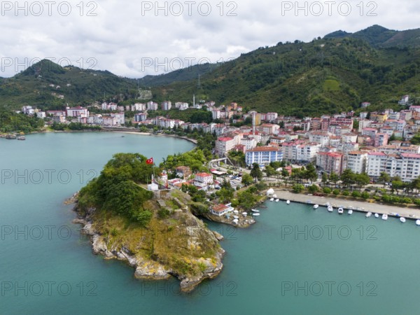 Coastal town with mountains and green hill, Turkish flag on a small cape, aerial view, fortress,