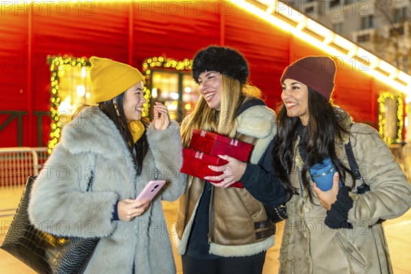 Three cheerful young women holding christmas gifts, enjoying christmas market at night, winter