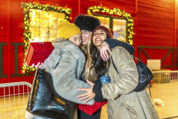 Three happy female friends are hugging at a christmas market at night, enjoying the festive