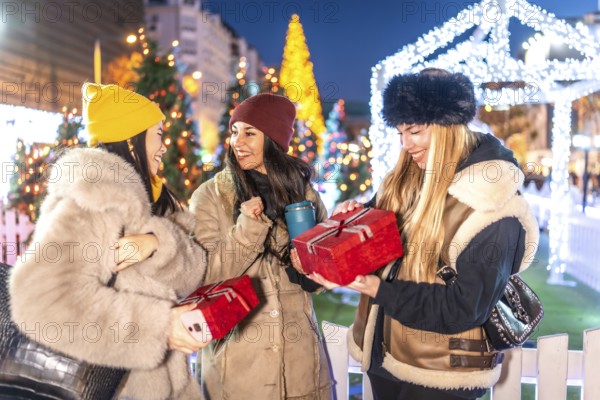 Three joyful women exchanging christmas gifts in a beautifully decorated city square, surrounded by