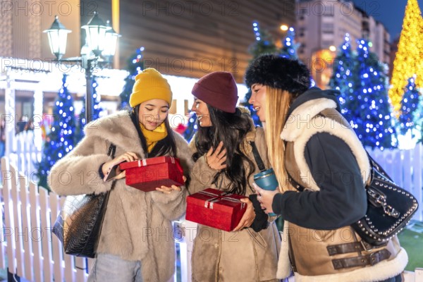 Cheerful young women exchanging christmas gifts at a decorated christmas market in the city at